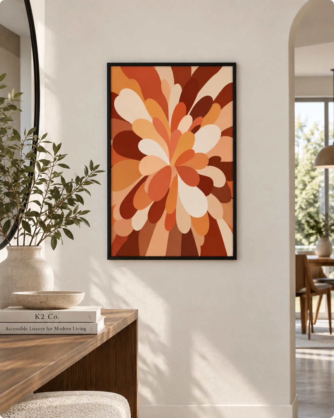 A framed abstract floral wall art print hangs on a white wall in a modern interior setting with a wooden console table, books, a vase with greenery, and an arched doorway in the background.