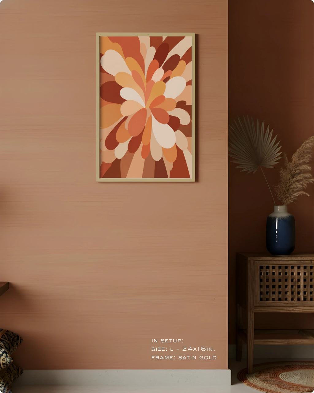 A framed abstract floral art print in warm earth tones hangs on a terracotta-colored wall in a styled interior setting with a wooden side table, blue vase, dried palm leaves, and a rug.