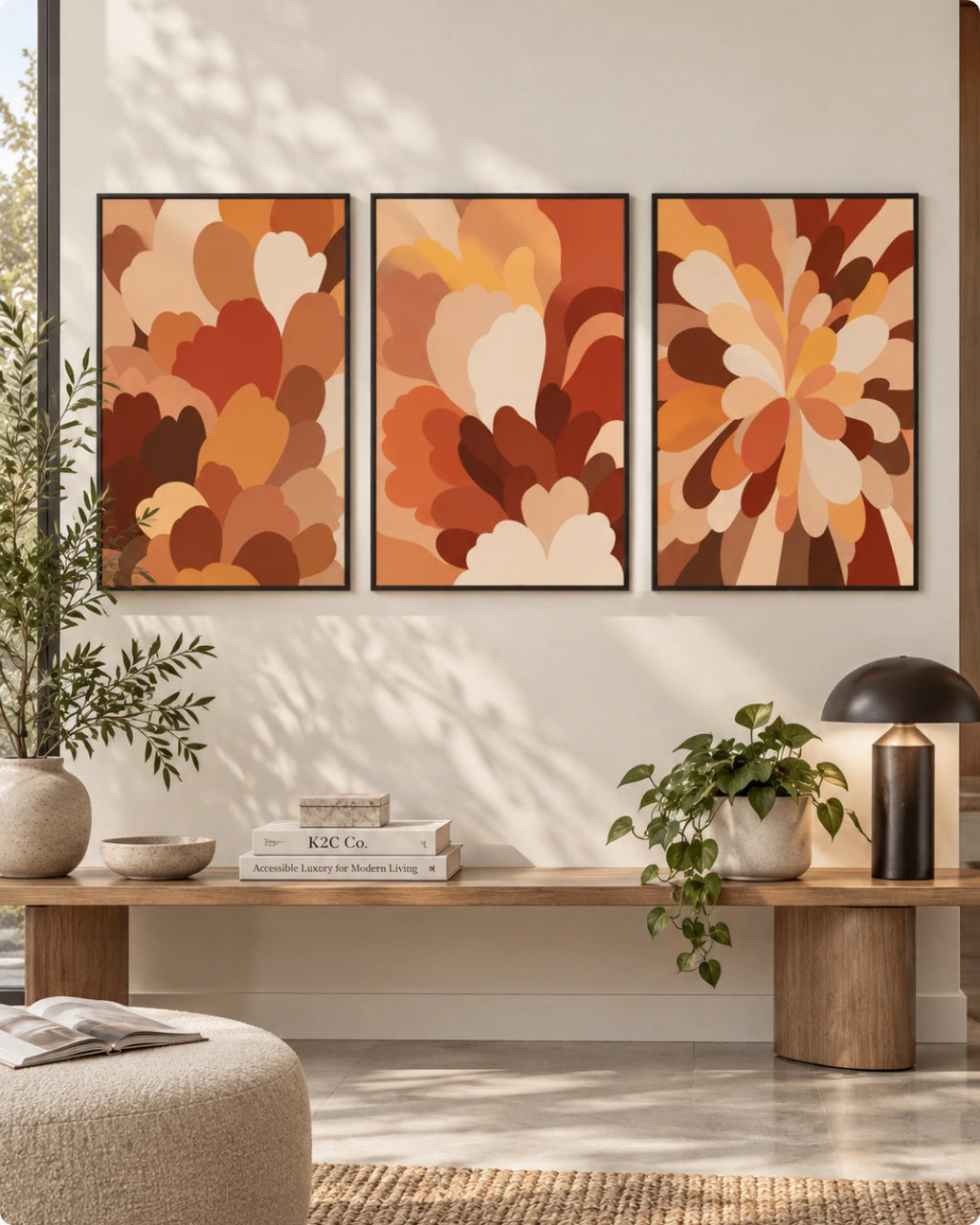 A three-panel framed abstract wall art set hangs above a wooden bench in a styled living room. The artwork features layered organic floral or petal-like shapes in warm autumn tones including rust, terracotta, orange, tan, cream, and brown.
