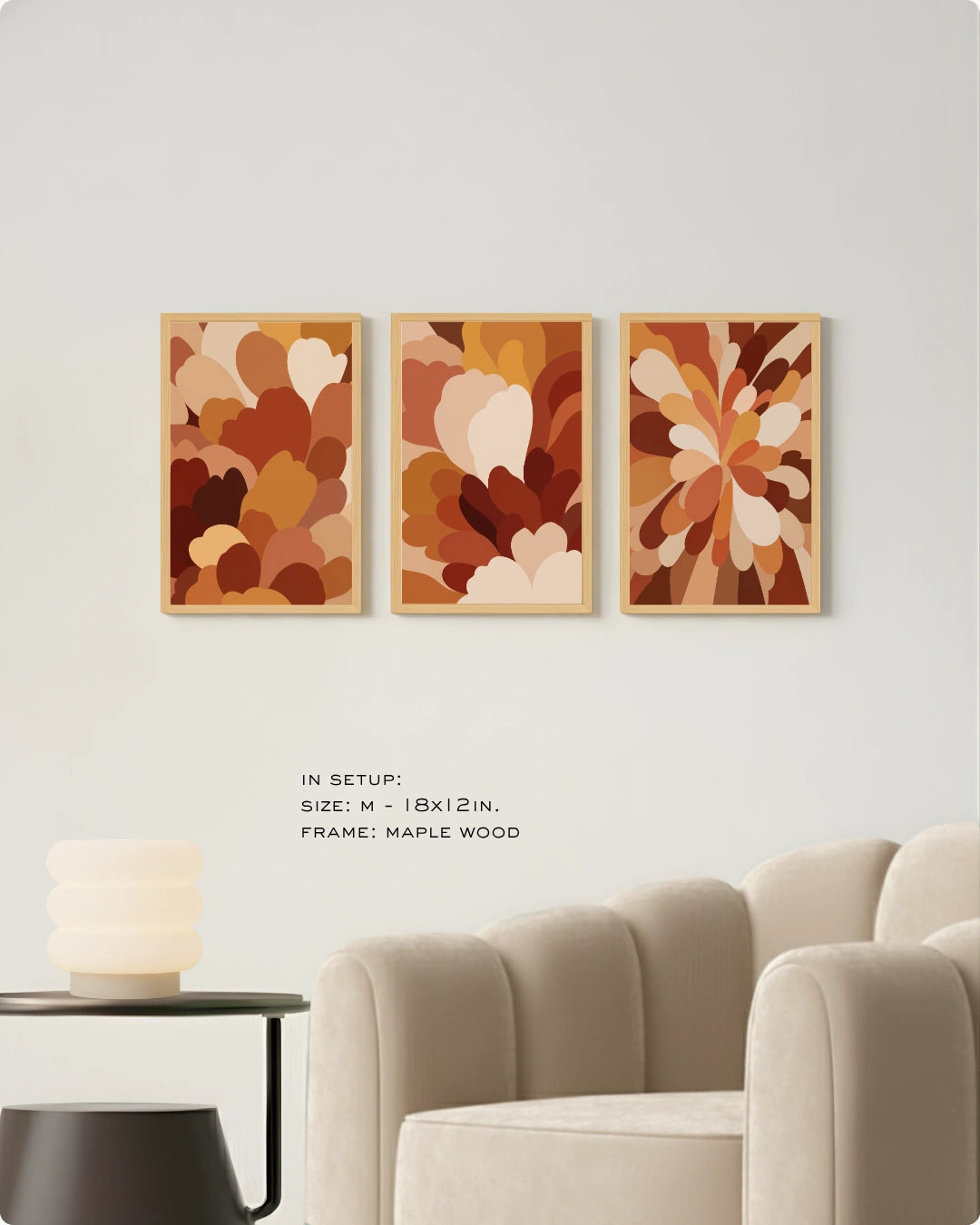 Three framed abstract floral art prints in warm earthy tones displayed on a white wall above a beige armchair, with small text noting size and maple wood frame.