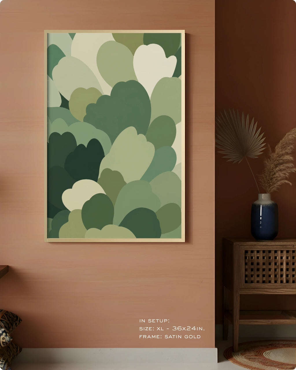 A framed abstract wall art print with layered green and cream cloud-like shapes, displayed on a warm terracotta wall in a styled interior setting with a side table and vase.
