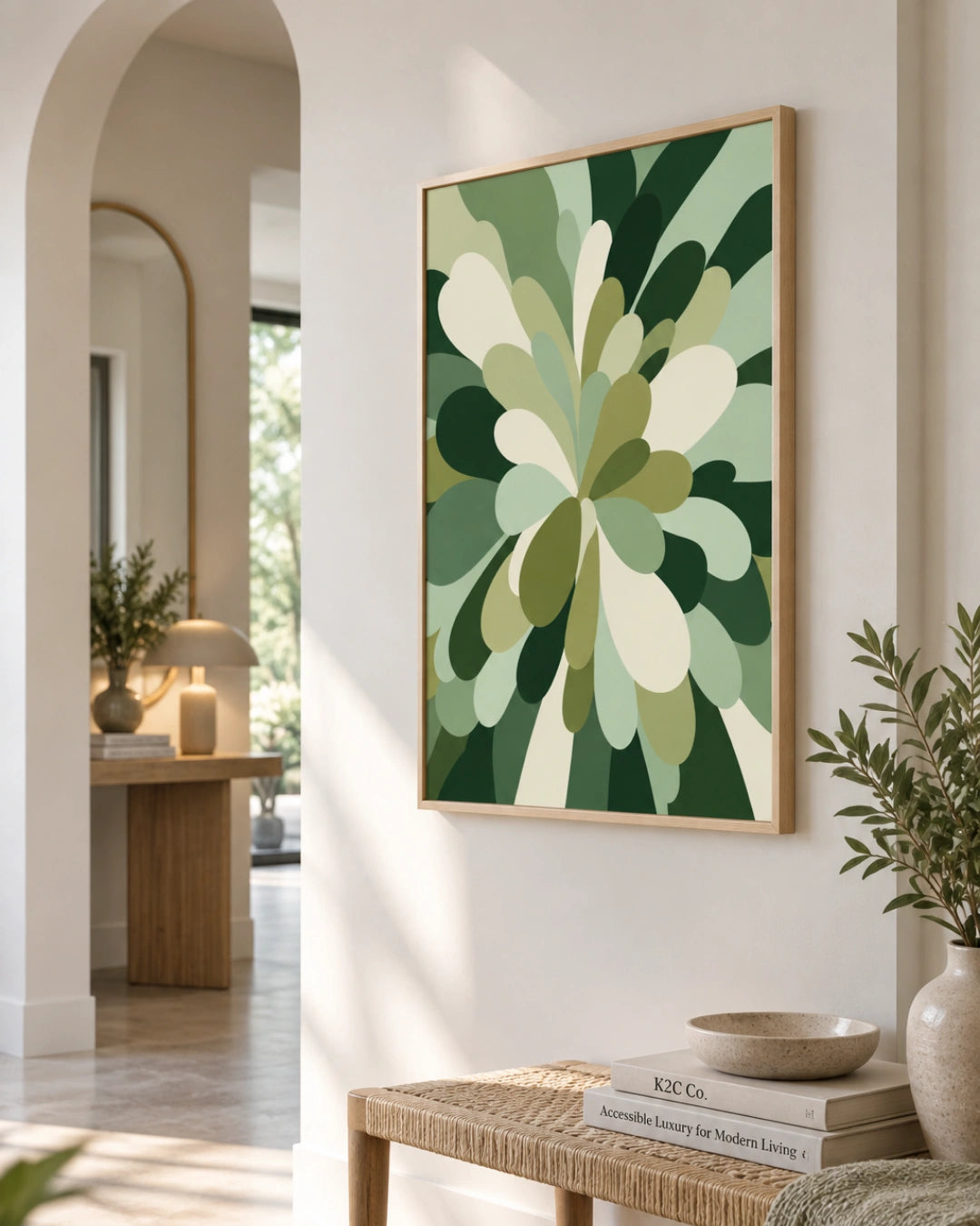 A framed abstract botanical art print with layered green and cream leaf-like shapes hanging on a warm beige wall in a styled interior hallway with a bench, books, and plants.