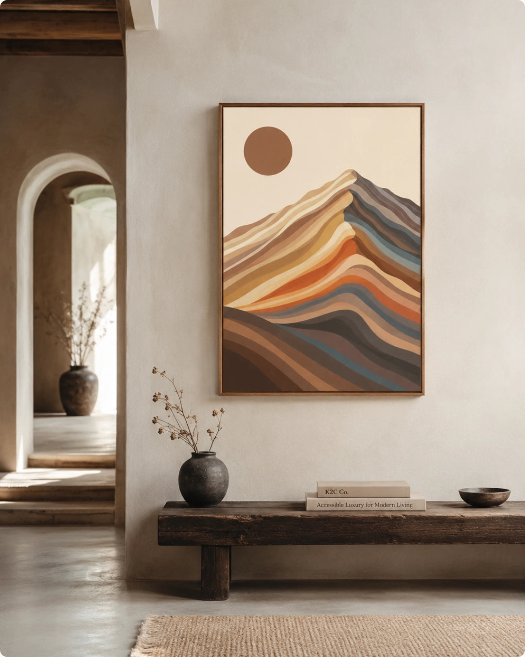 A framed abstract landscape art print featuring layered mountain-like hills and a sun in warm earthy tones, displayed on a light wall above a wooden cabinet in a styled interior room.