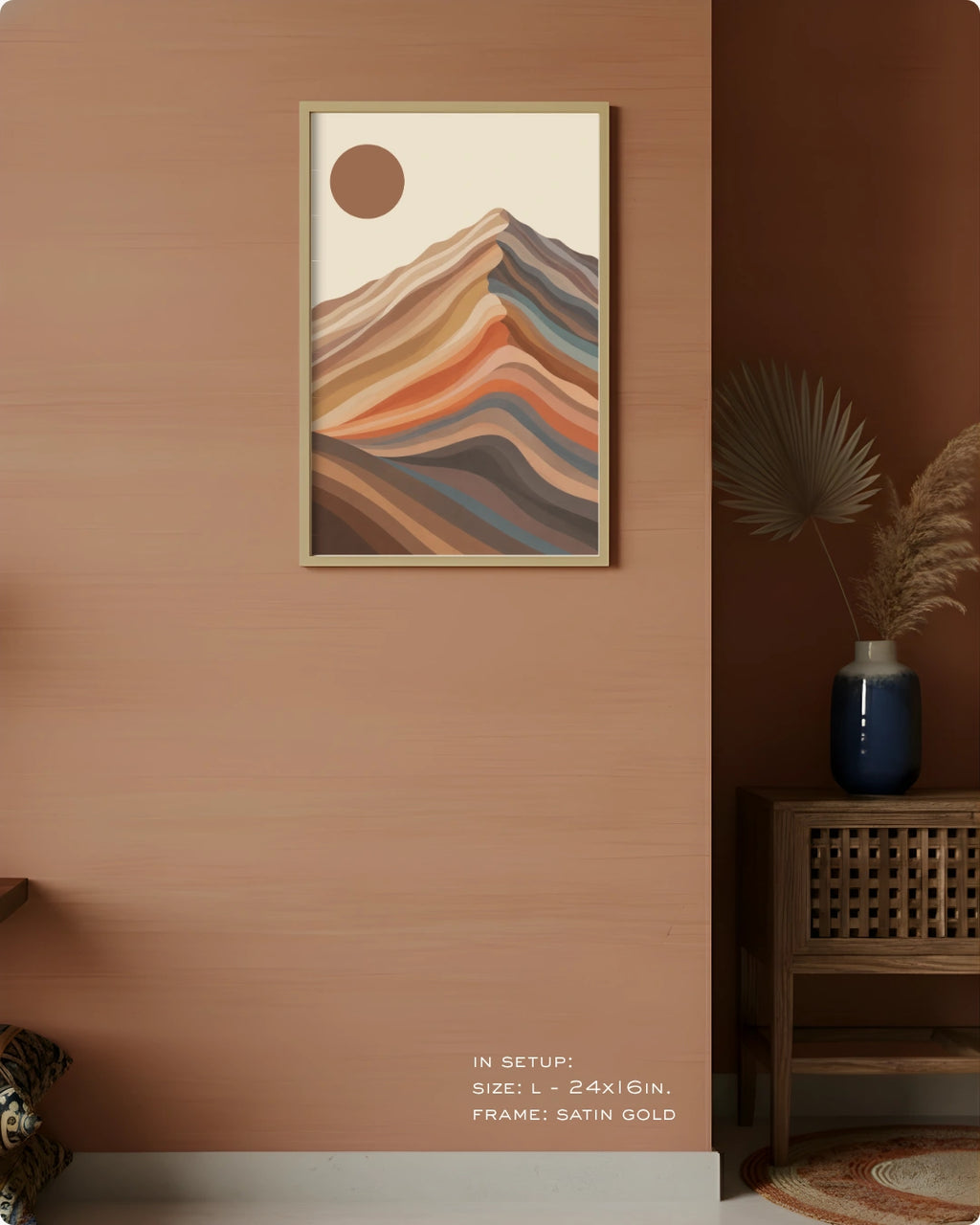 A framed abstract landscape art print featuring layered mountain-like hills and a sun in warm earthy tones, displayed on a light wall above a wooden cabinet in a styled interior room.