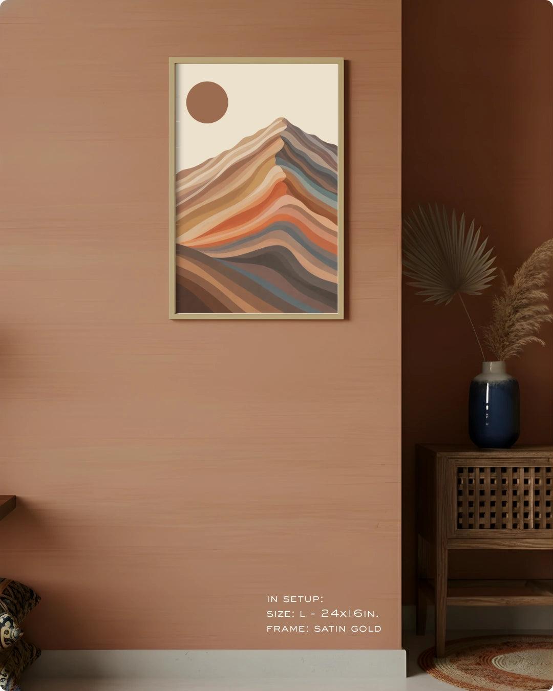 A framed abstract landscape art print featuring layered mountain-like hills and a sun in warm earthy tones, displayed on a light wall above a wooden cabinet in a styled interior room.