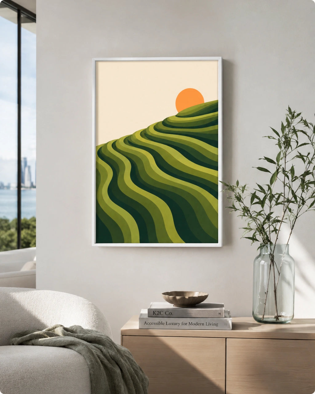 A framed art print featuring a stylized green rolling hill landscape with a small orange sun on a cream background, displayed on a light gray wall in a modern living room setting.
