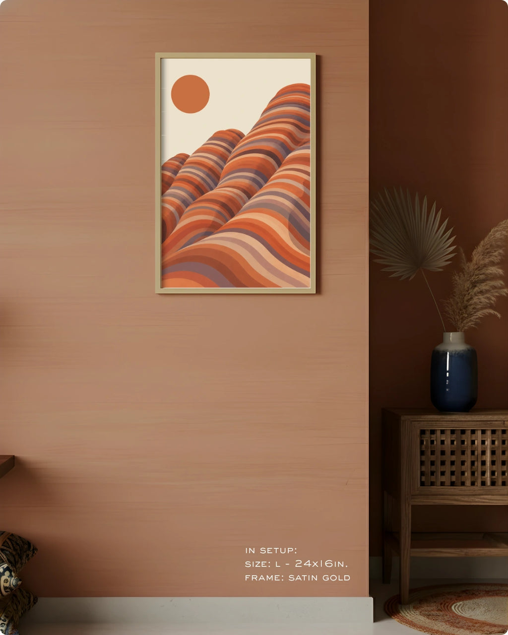 A framed art print featuring a retro-style illustration of wavy orange and terracotta hills under a solid orange sun, displayed on a warm terracotta wall in a styled interior setting.