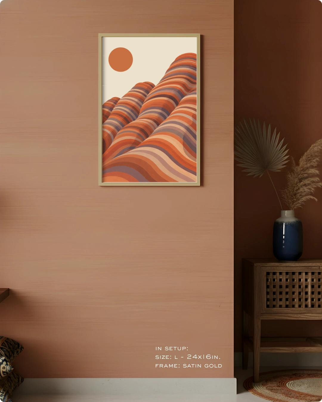 A framed art print featuring a retro-style illustration of wavy orange and terracotta hills under a solid orange sun, displayed on a warm terracotta wall in a styled interior setting.