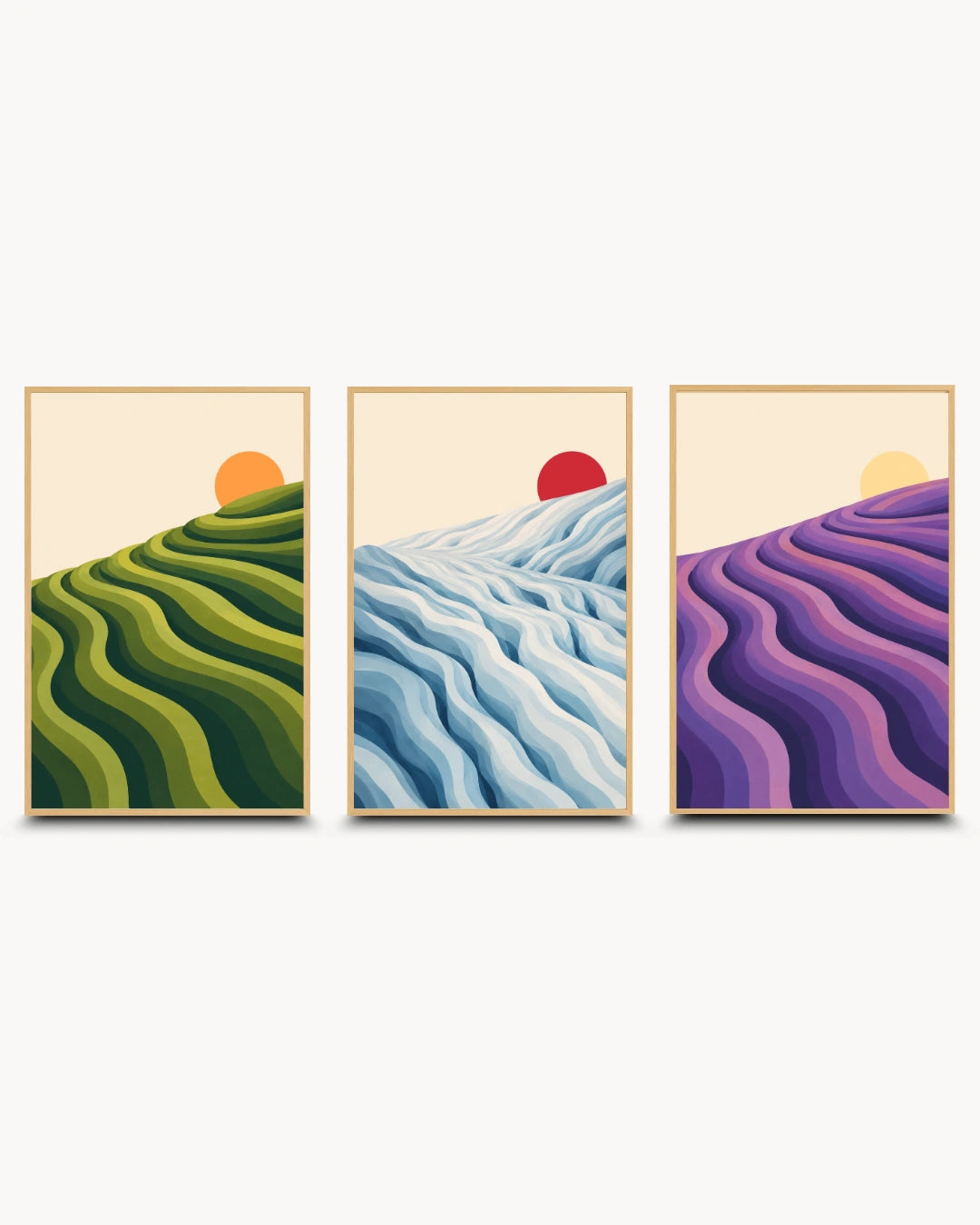 A three-panel framed wall art set showing stylized landscape scenes: green rolling hills with an orange sun, blue and white wavy terrain with a red sun, and purple rolling hills with a yellow sun, displayed against a light gray background.