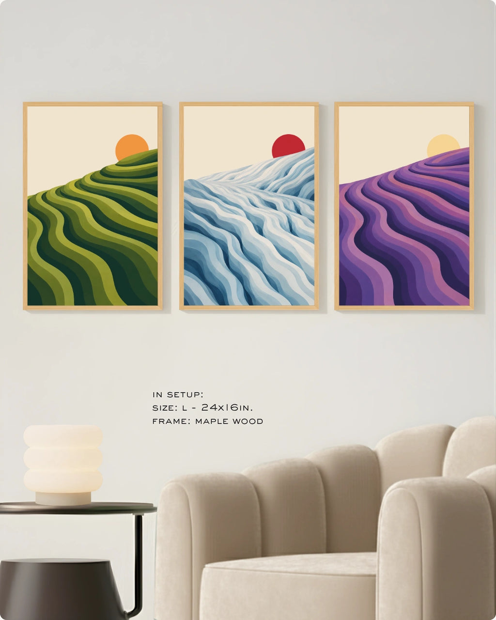 Three framed landscape art prints hang on a light gray wall above a beige armchair and side table. The prints show stylized wavy hillside patterns in green, blue, and purple with small orange and red sun motifs.