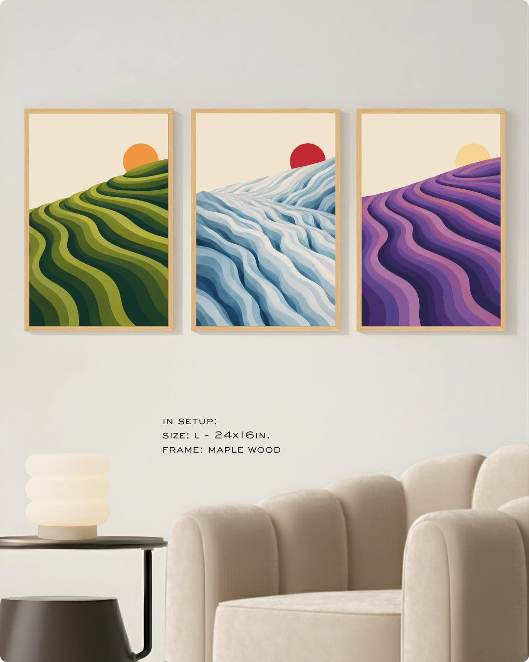Three framed landscape art prints hang on a light gray wall above a beige armchair and side table. The prints show stylized wavy hillside patterns in green, blue, and purple with small orange and red sun motifs.