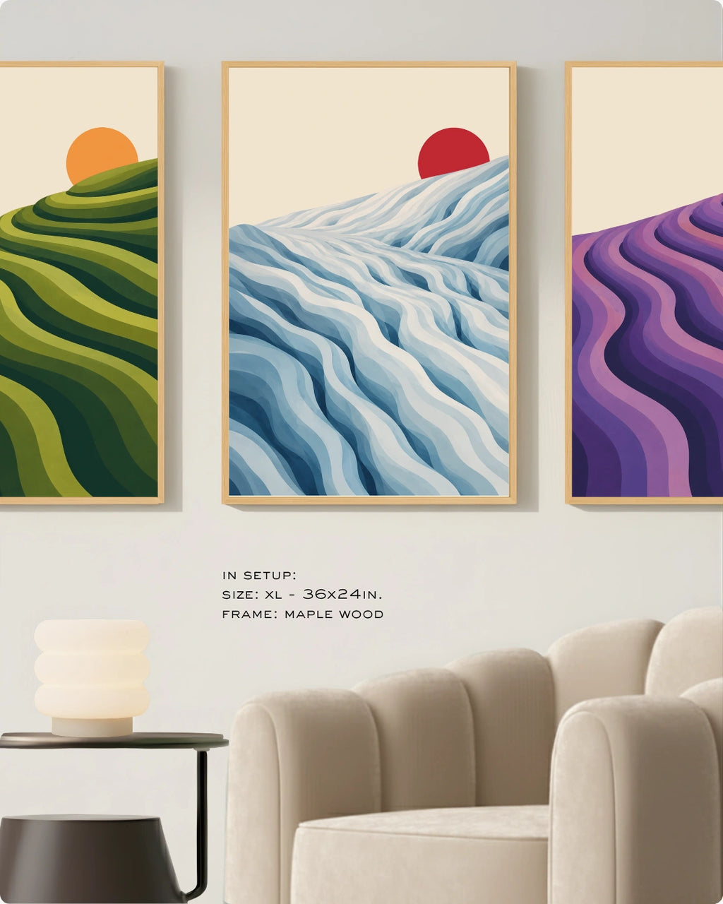 Three framed abstract landscape wall art prints hang above a beige armchair in a styled interior. The center print shows blue and white wavy hills with a red sun, the left print shows green rolling hills with an orange sun, and the right print shows purple wavy hills.