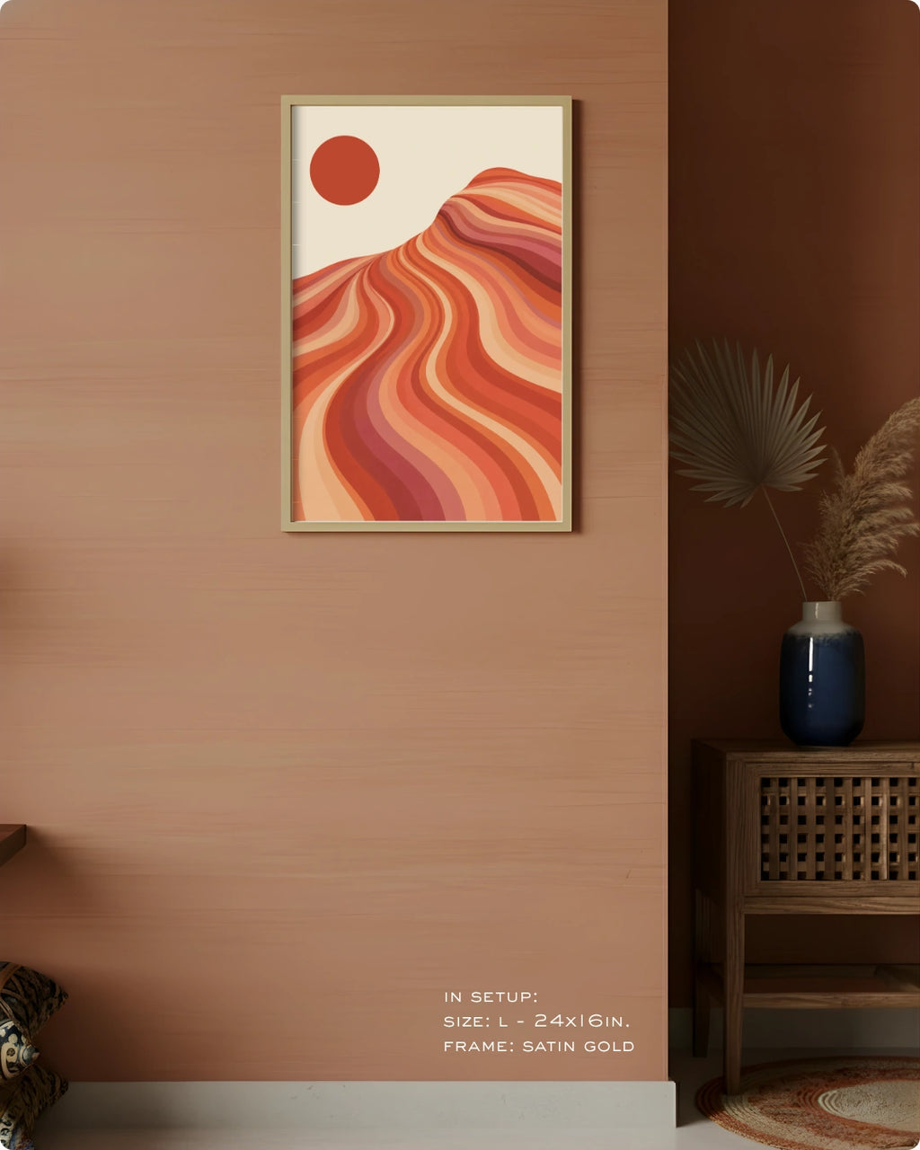 A framed abstract landscape art print featuring wavy orange and red hills under a red sun on a cream background, styled on a warm terracotta wall in a modern interior setting.