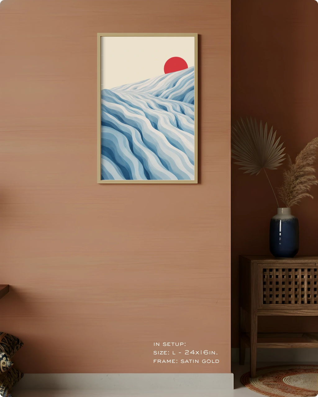 A framed wall art print hangs on a warm peach wall in a styled interior. The artwork shows layered blue and white wavy hills with a red sun on a cream background.