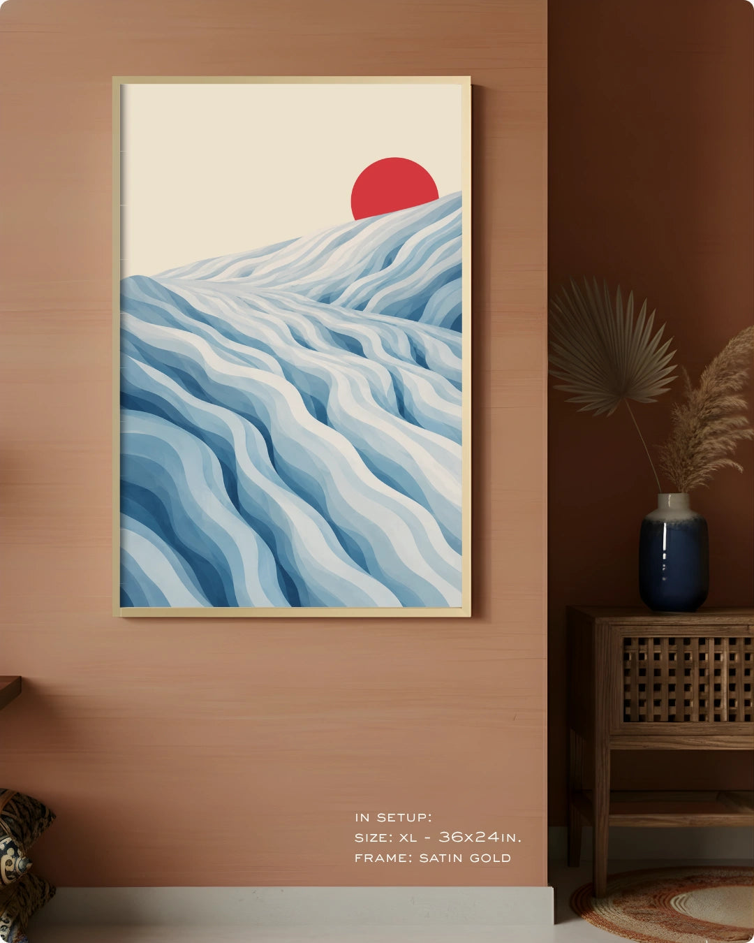 A framed art print featuring a stylized landscape with layered blue and white waves and a red sun on a cream background, displayed on a warm brown wall in a styled interior setting.