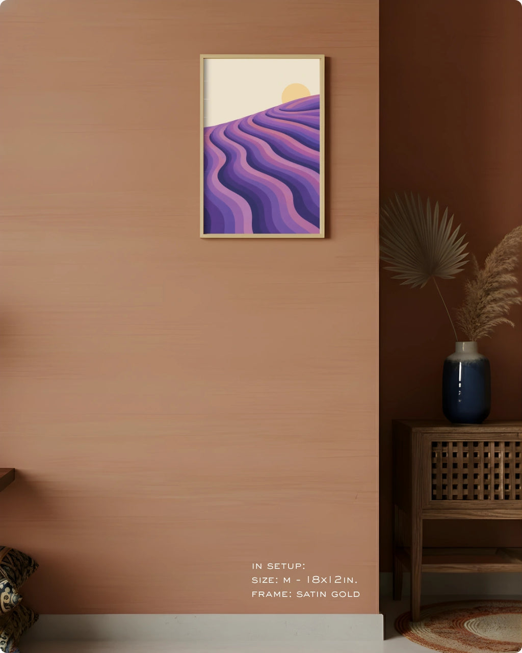 A framed wall art print hangs on a terracotta-colored wall in a styled interior. The artwork shows abstract wavy purple and lavender hills under a pale cream sky with a small yellow sun.