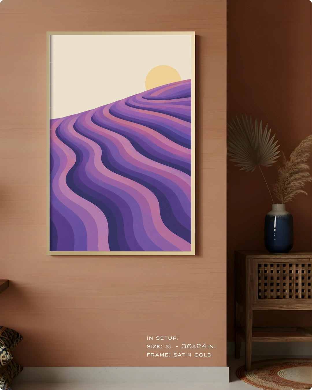 A framed abstract landscape art print featuring purple and lavender wavy hills under a pale yellow sun, displayed on a warm brown wall in a styled interior setting.