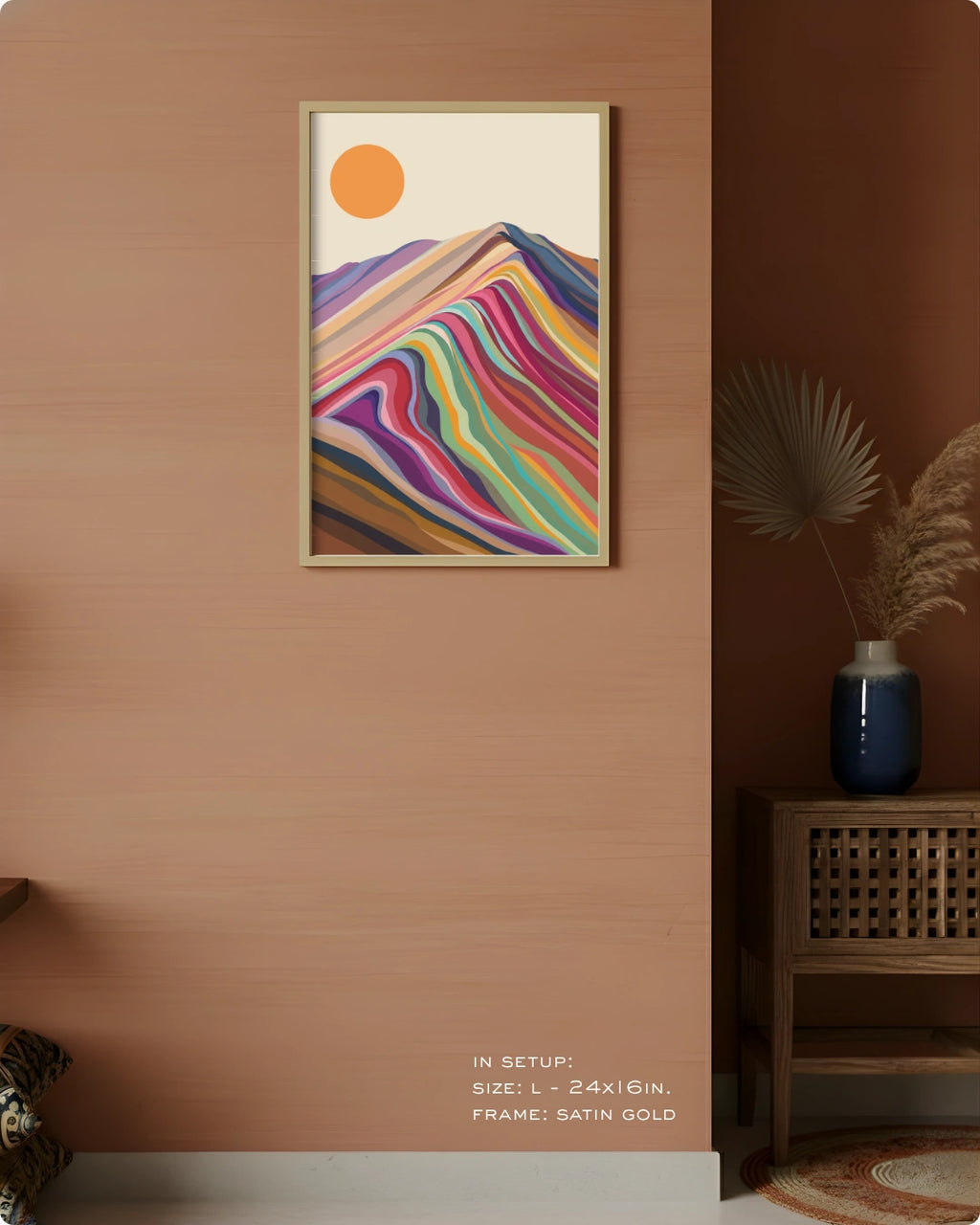 A framed vertical art print featuring a colorful abstract mountain landscape with a bright orange sun, displayed on a warm peach wall in a styled interior setting.