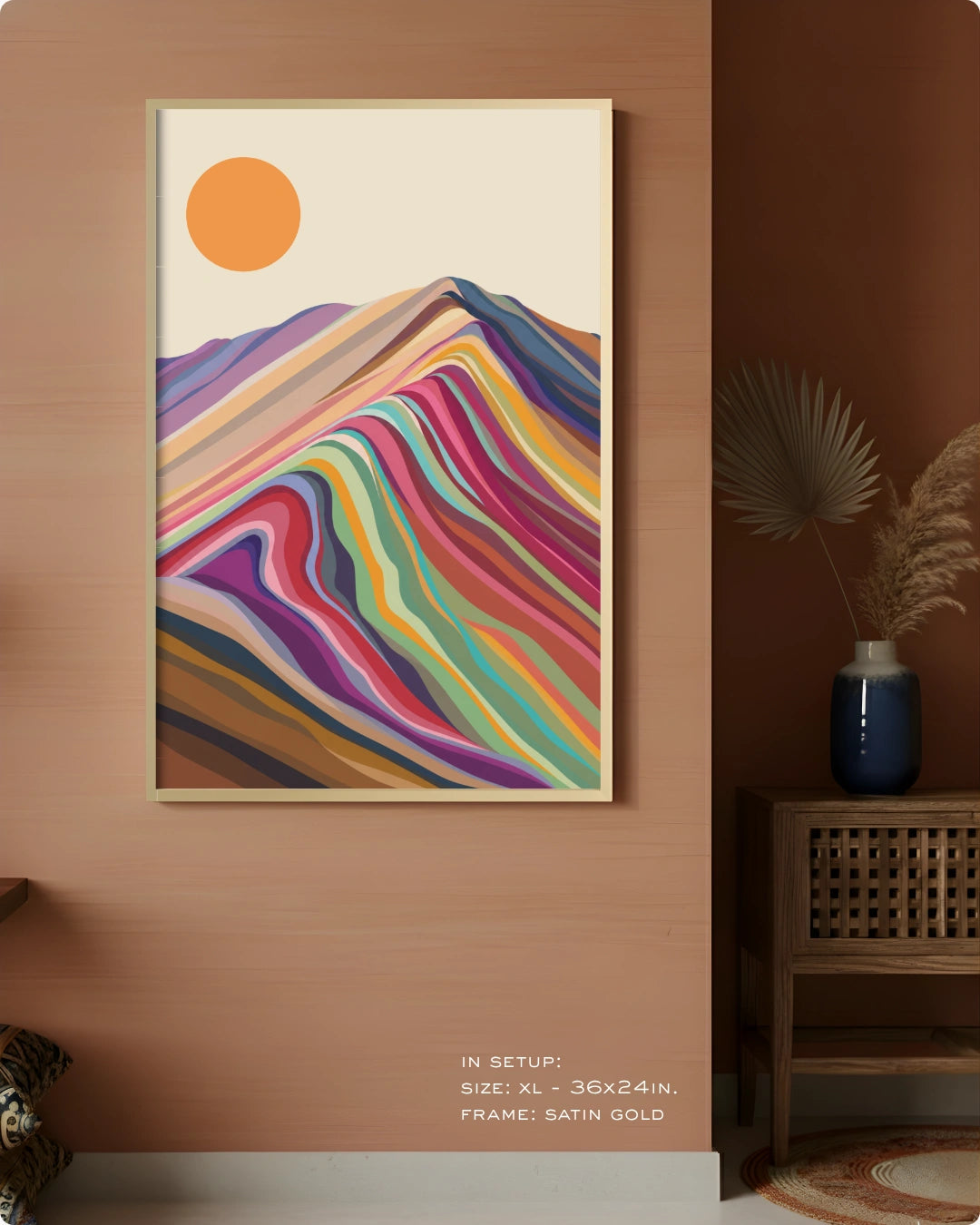 A framed abstract art print featuring colorful wavy mountain-like stripes and an orange sun on a cream background, displayed on a white wall in a modern home office setting with a desk, chair, and bookshelf.