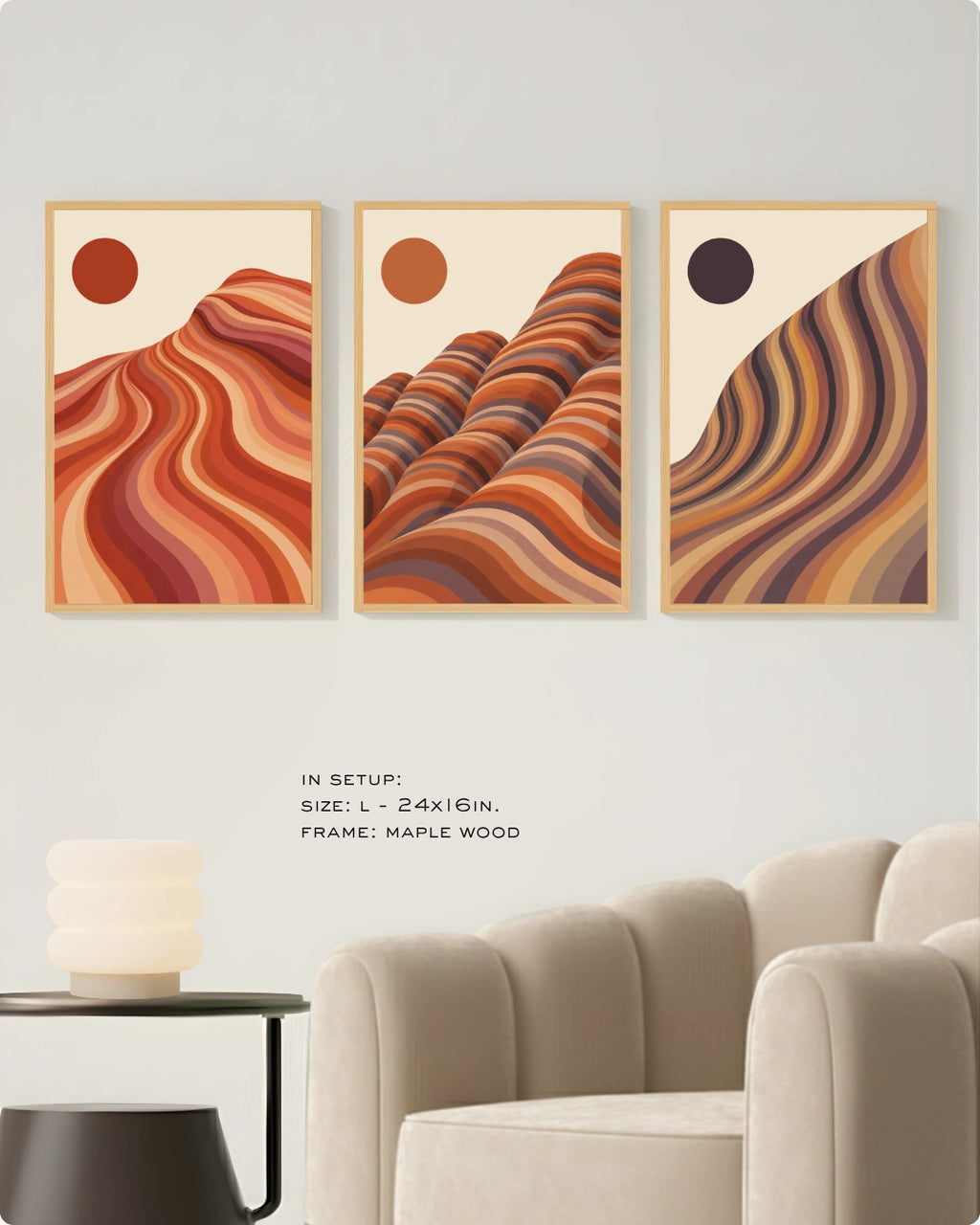 Three framed abstract wall art prints hang on a light wall above a beige sofa, showing layered wavy mountain-like forms in warm orange, red, brown, and cream tones. Small text below reads 'IN SETUP: SIZE: L-24x16in.