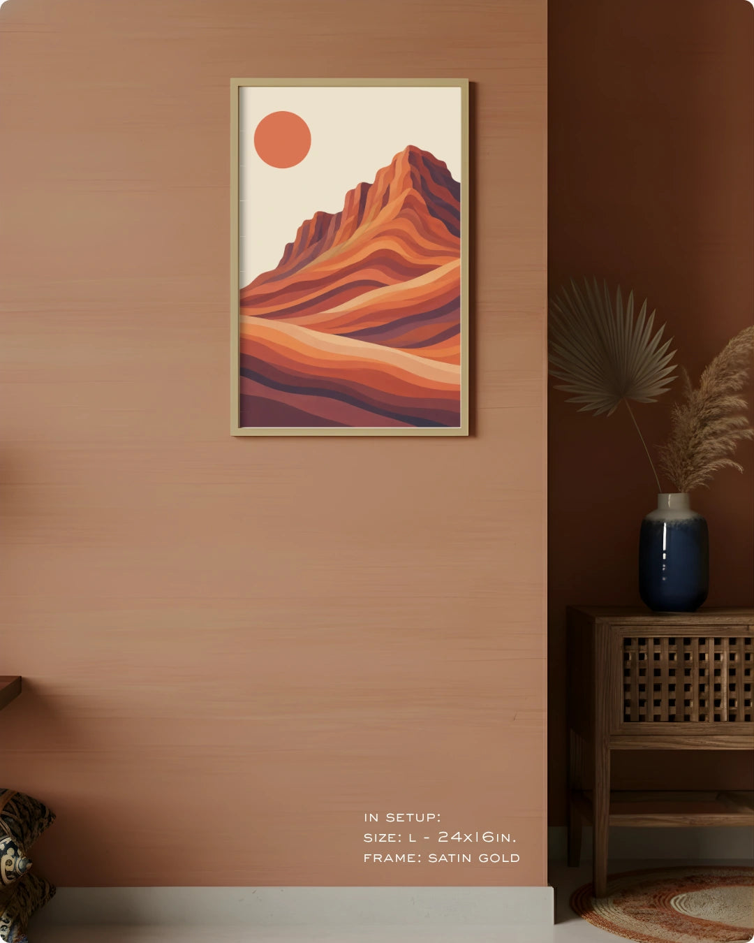 A framed art print depicting a stylized desert mountain landscape with a sun, displayed on a warm terracotta wall in a styled interior setting.