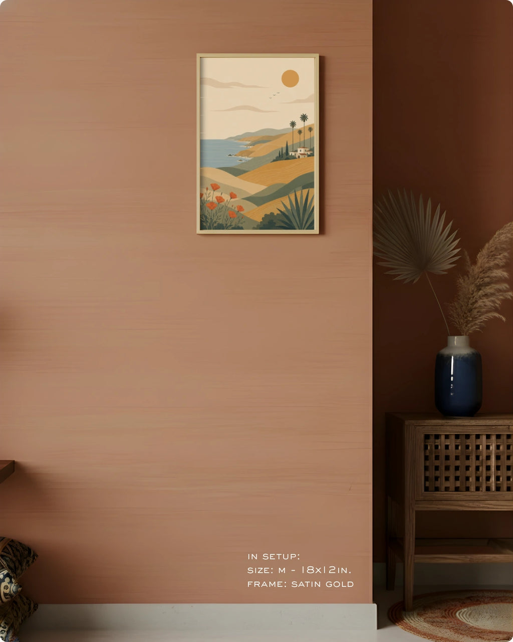 A framed landscape art print hangs on a warm terracotta wall in a styled interior setting. The print features a retro coastal scene with hills, palm trees, a small boat, and a sun.
