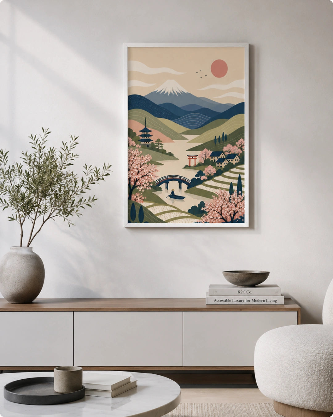 A framed art print featuring a stylized Japanese landscape with Mount Fuji, cherry blossoms, a pagoda, and a bridge, displayed on a white wall above a modern console table in a styled living room.