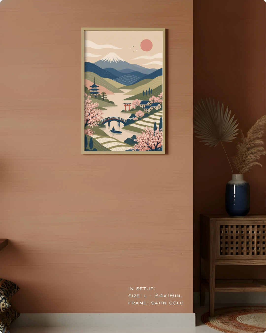 A framed art print featuring a stylized Japanese landscape with Mount Fuji, cherry blossoms, and a bridge, displayed on a warm terracotta wall in a styled interior setting.