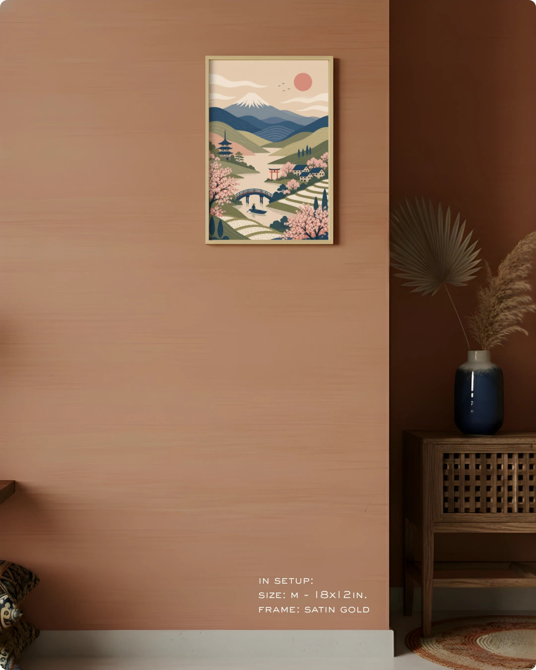 A framed art print featuring a stylized Japanese landscape with mountains, cherry blossoms, and a river, displayed on a warm terracotta wall in a styled interior setting.