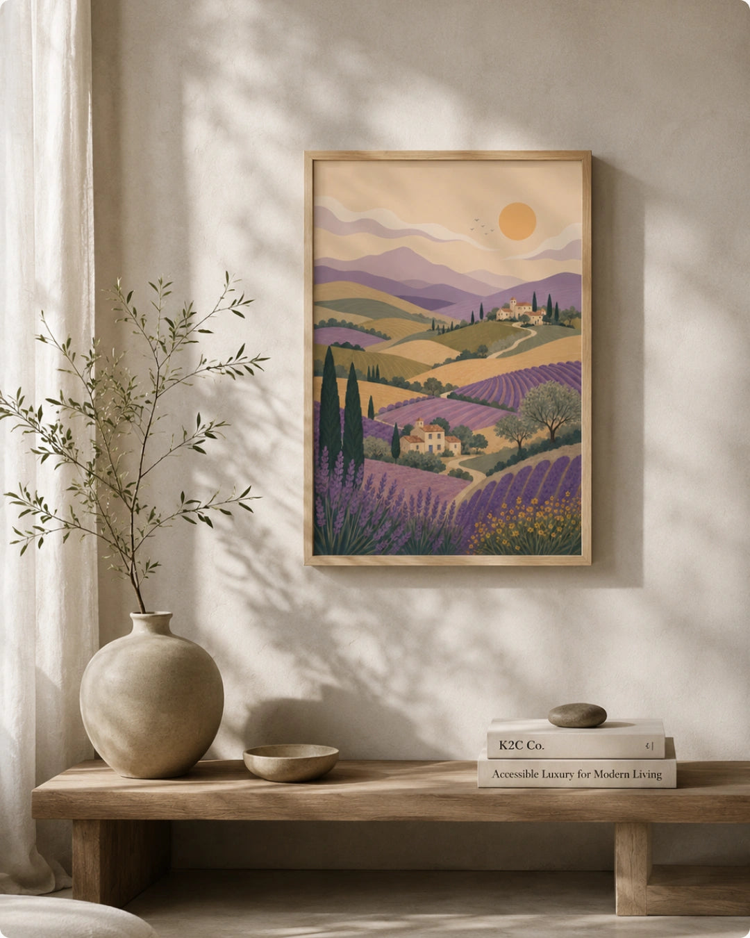 A framed art print of a lavender field landscape in Provence, featuring purple hills, cypress trees, and a yellow sun, styled on a beige wall above a wooden console table with a vase and books.