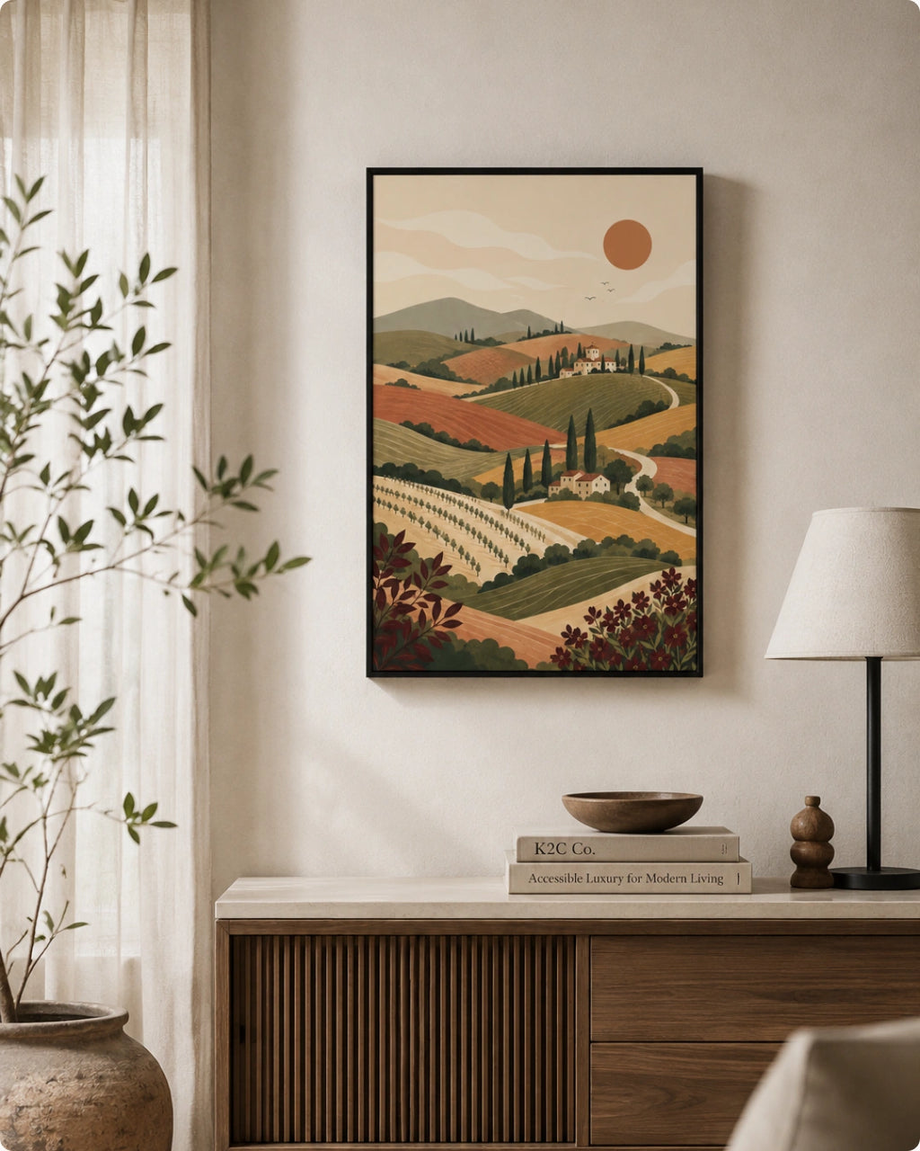 A framed art print of a Tuscan vineyard landscape hangs on a beige wall above a wooden console table in a styled room setting with a lamp, books, and a potted plant.