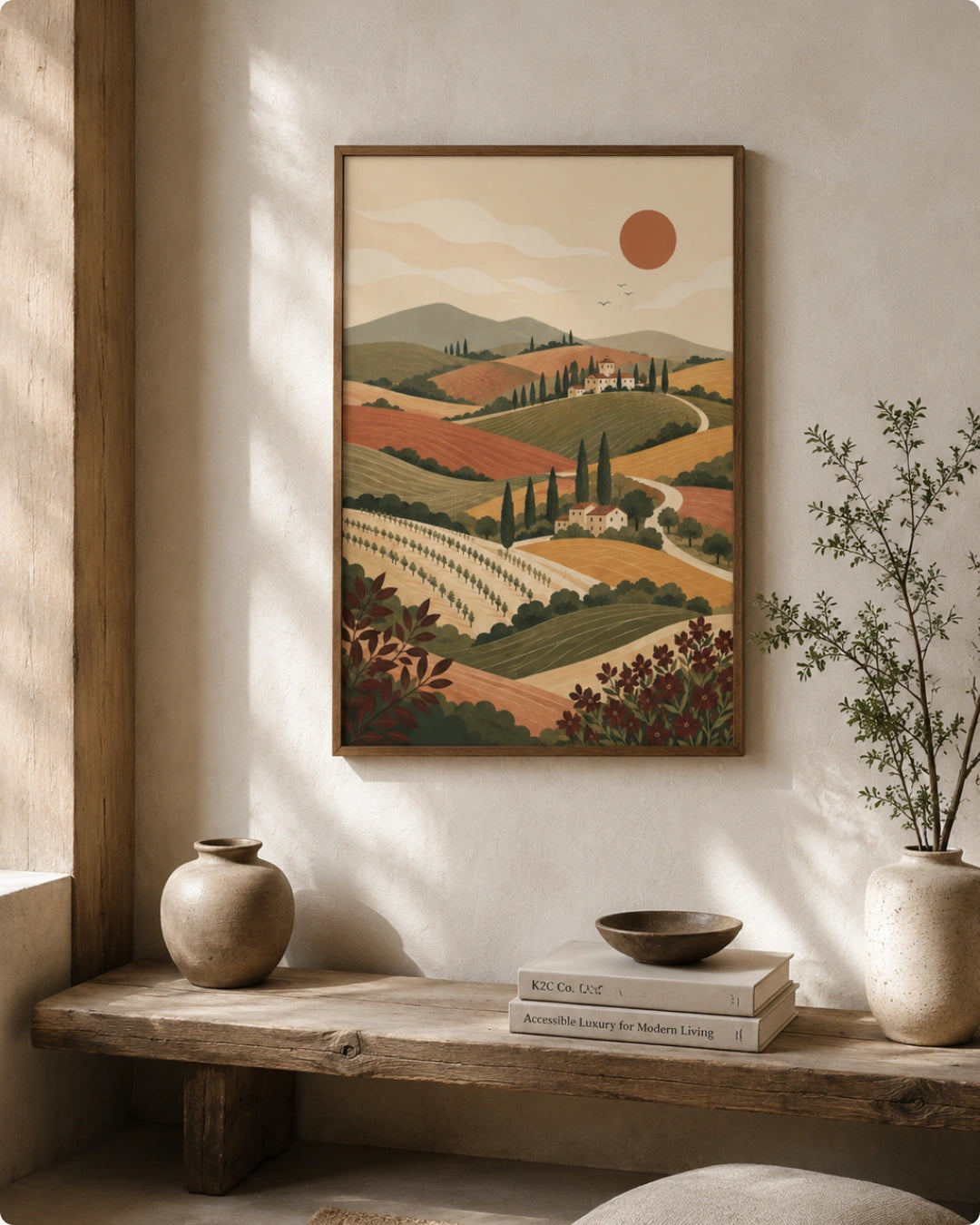 A framed landscape art print featuring a Tuscany vineyard and rolling hills under a warm sun, styled on a textured wall above a rustic wooden bench with decorative vases and books.