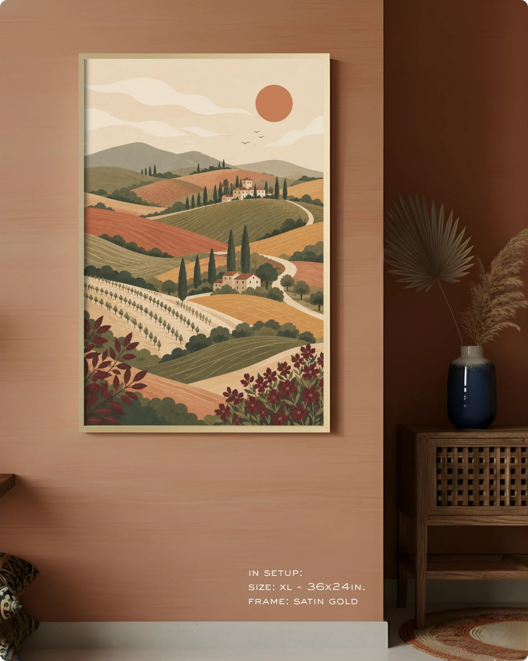 A framed landscape art print depicting rolling vineyard hills under a warm sun, displayed on a terracotta-colored wall in a styled interior setting.