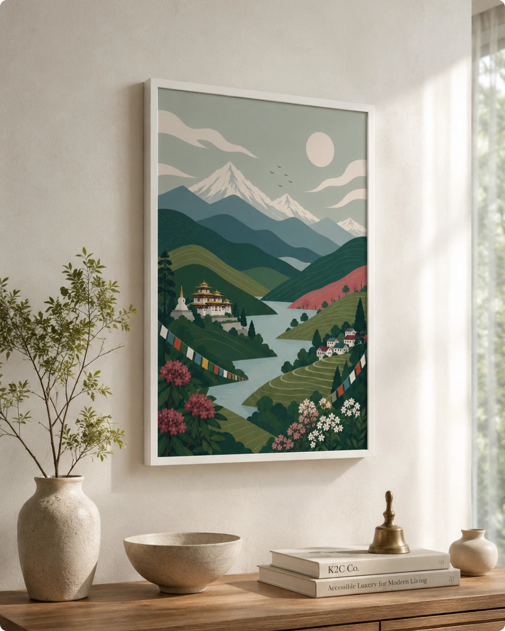 A framed art print depicting a stylized mountain landscape with a lake, green hills, and a monastery, displayed on a wall above a wooden console table with decorative items.