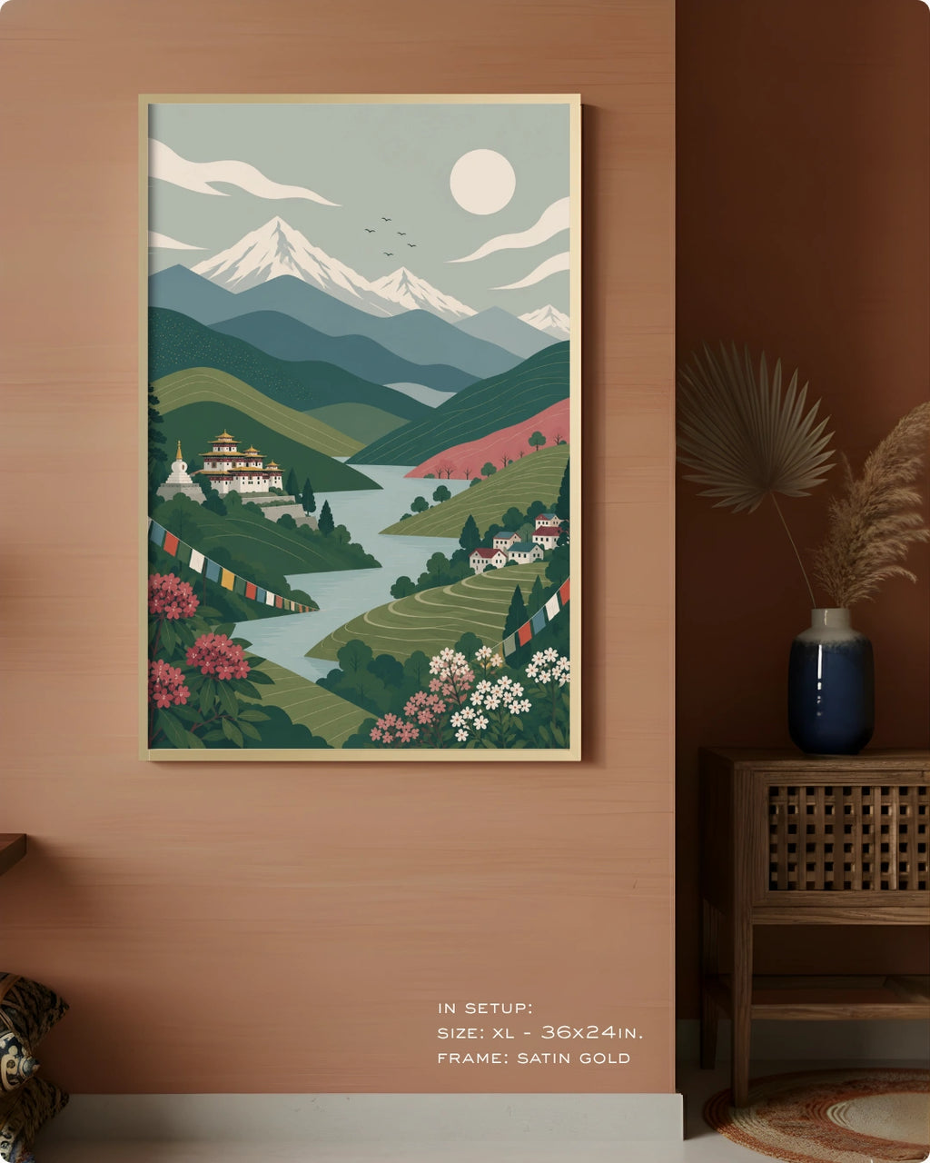 A framed art print depicting a stylized mountain landscape with a lake, hills, flowers, and a temple, displayed on a warm terracotta wall in a styled interior setting.
