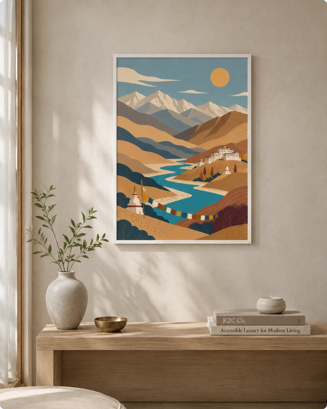 A framed art print featuring a stylized landscape of snow-capped mountains, a winding blue river, and a yellow sun, displayed on a beige wall above a wooden console table with a vase and books.
