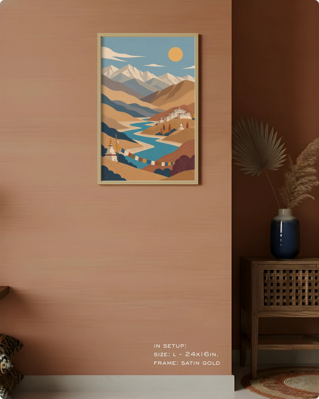 A framed art print featuring a stylized landscape with mountains, a winding river, and a yellow sun, displayed on a warm terracotta wall in a styled interior setting.