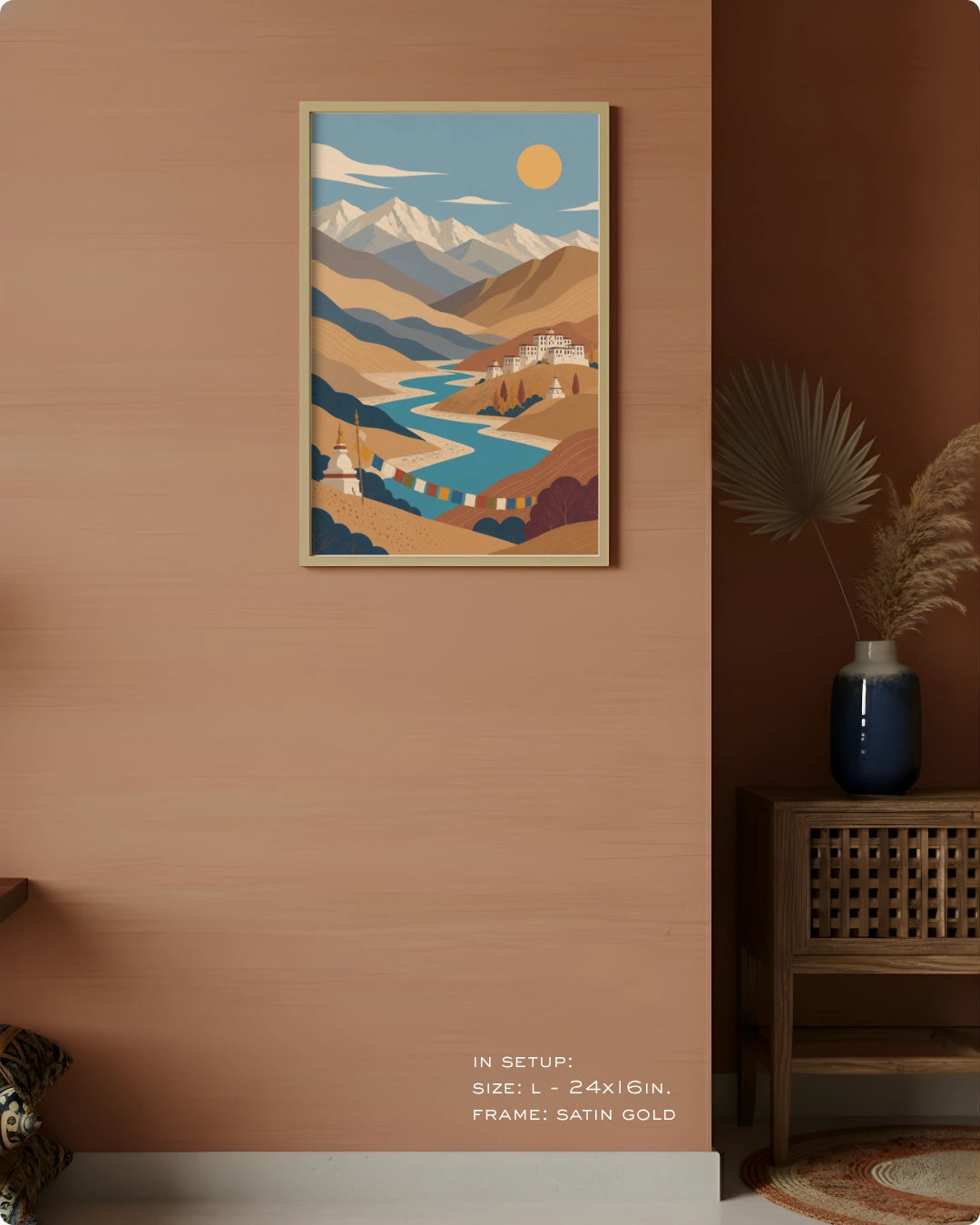 A framed art print featuring a stylized landscape with mountains, a winding river, and a yellow sun, displayed on a warm terracotta wall in a styled interior setting.