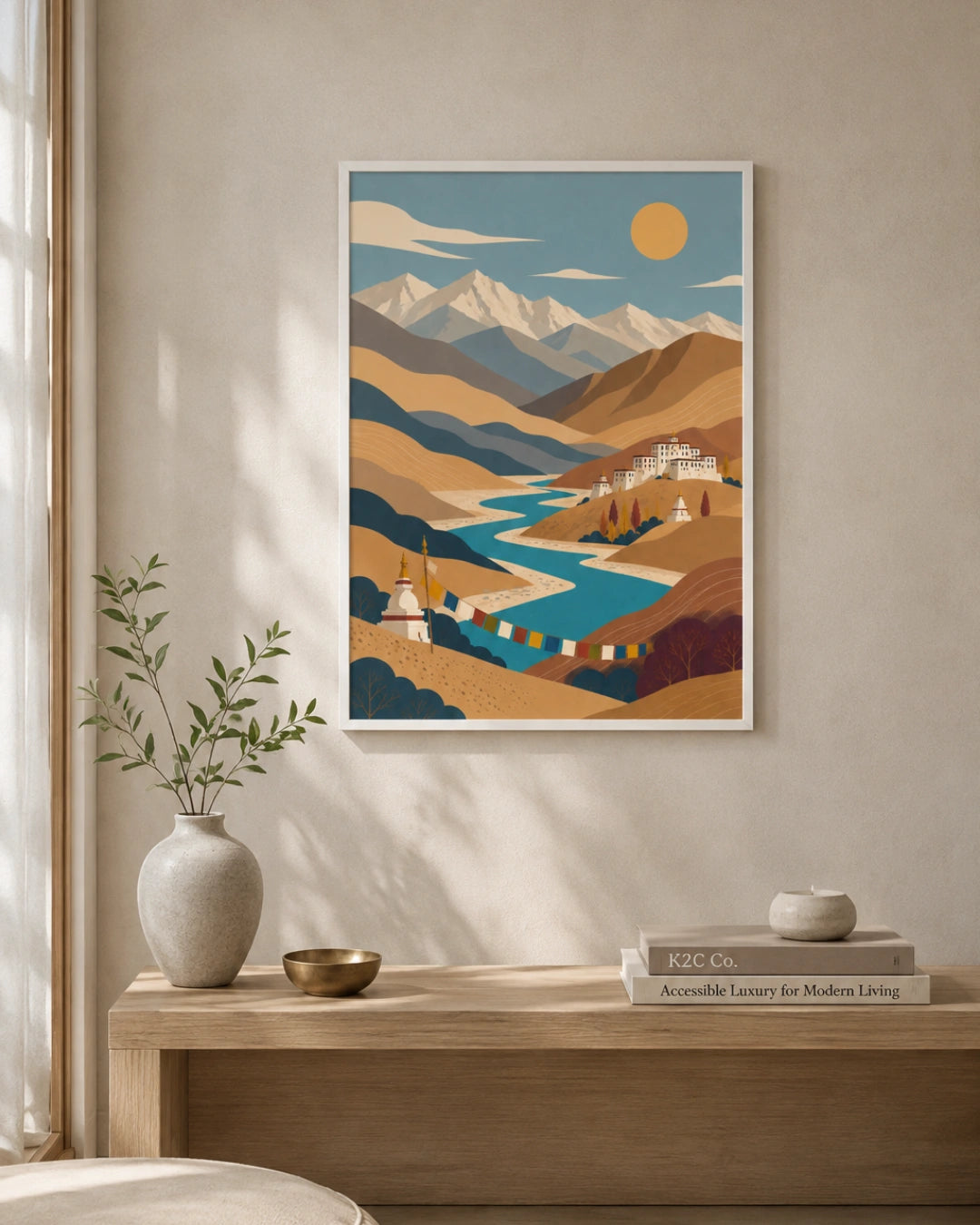 A framed art print featuring a stylized mountain landscape with a winding blue river, hanging on a beige wall above a wooden console table with a vase and books.