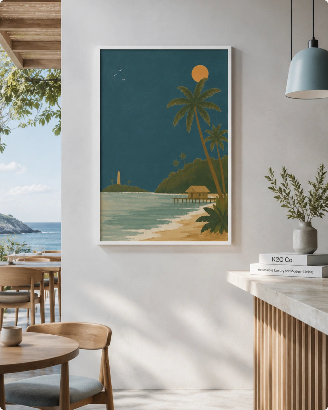 A framed art print featuring a tropical beach scene with palm trees, a lighthouse, and a yellow sun on a dark teal night sky, displayed on a white wall in a modern, sunlit interior with wooden furniture and a pendant light.