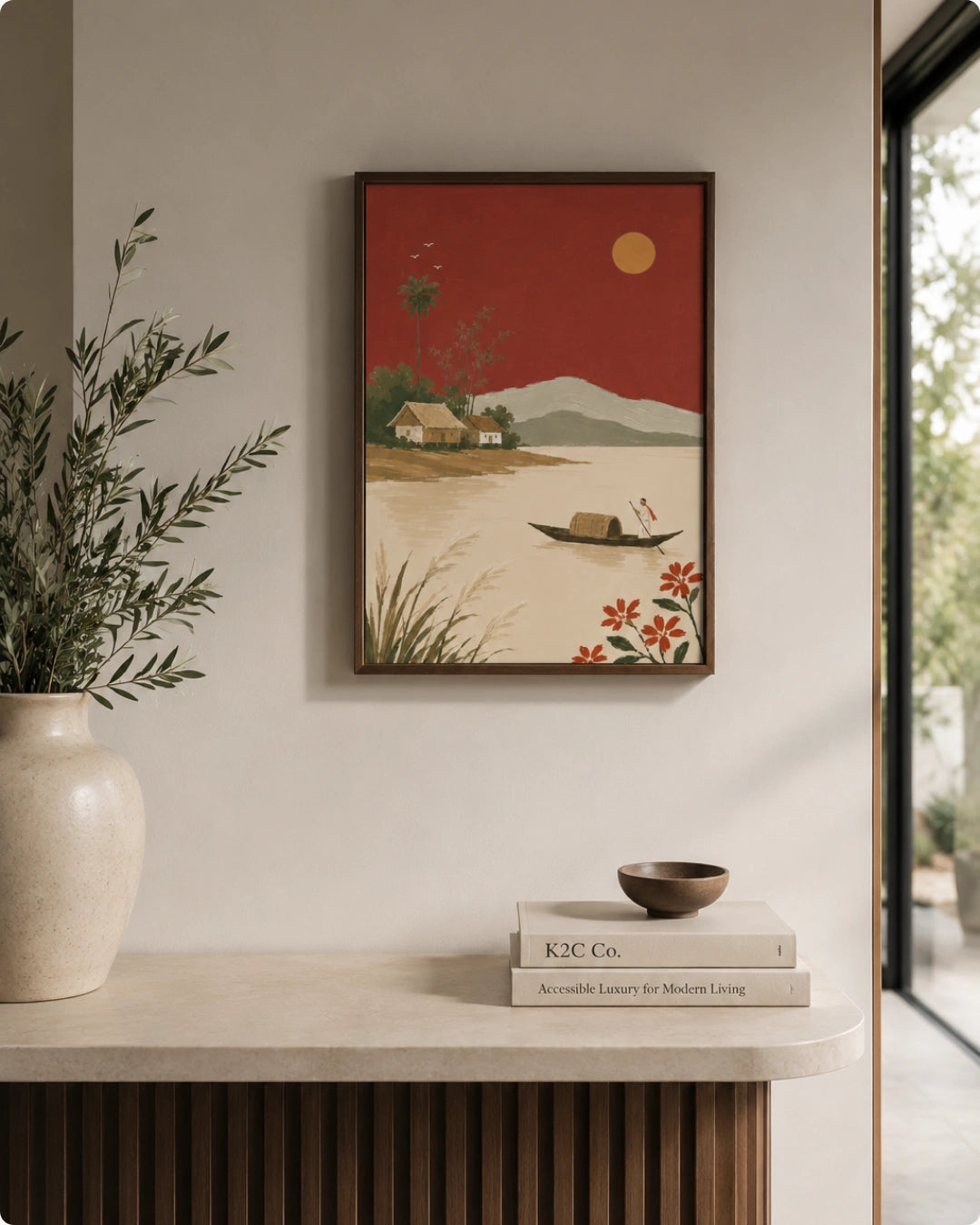 A framed art print depicting a serene landscape with a red sky, mountains, a boat, and flowers, styled on a beige wall above a console table with a vase and books.
