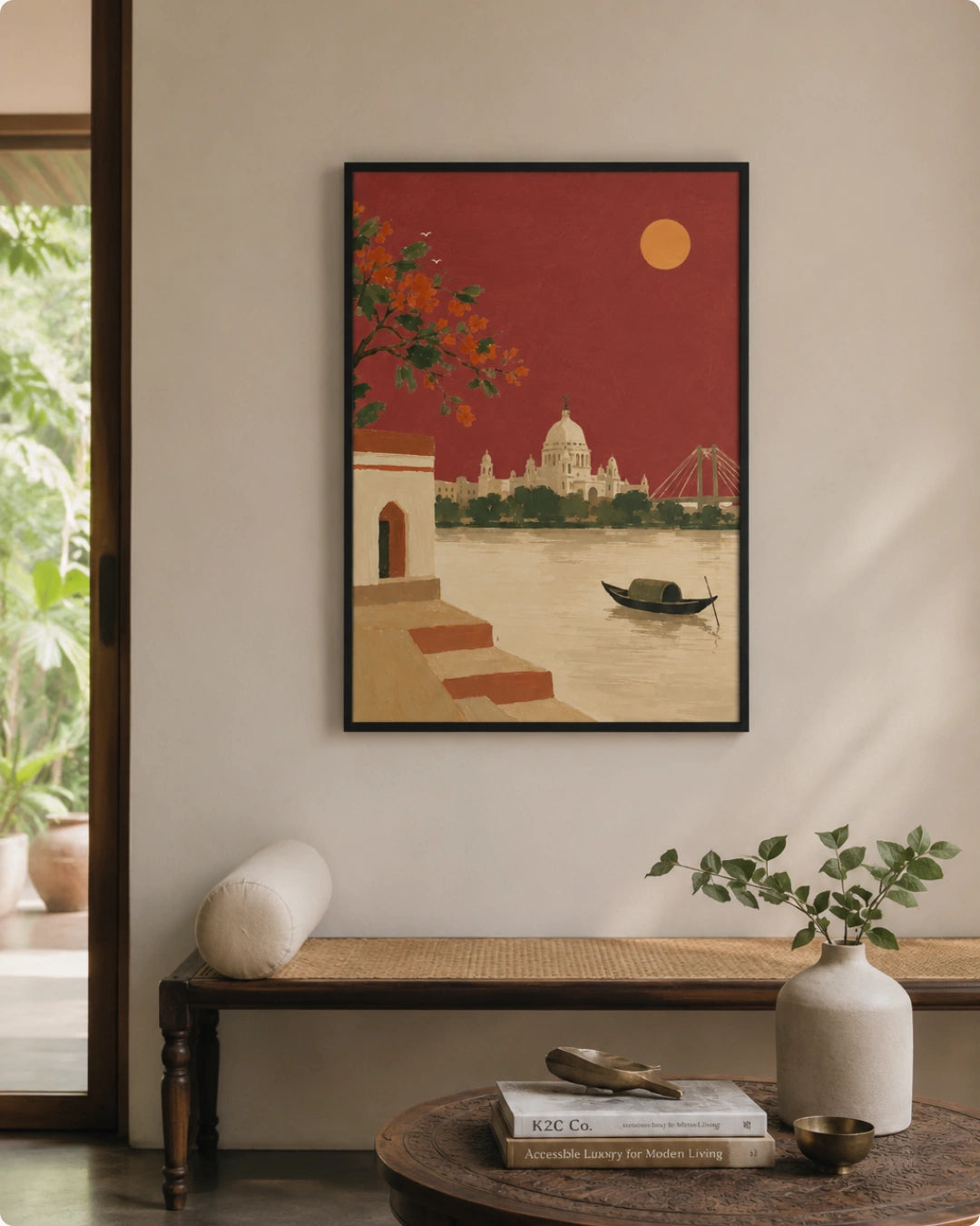 A framed vertical art print depicting a stylized red sunset over a river with domed architecture and a boat, displayed on a beige wall above a woven bench in a styled interior room.