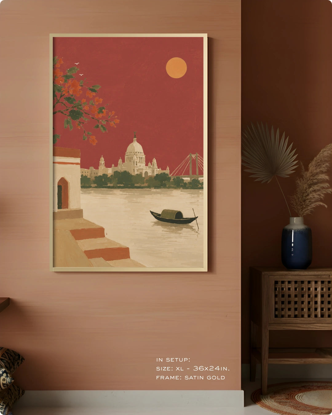 A framed art print depicting a scenic Indian cityscape with a domed cathedral, river, boat, and orange foliage, displayed on a warm terracotta wall in a styled interior setting.