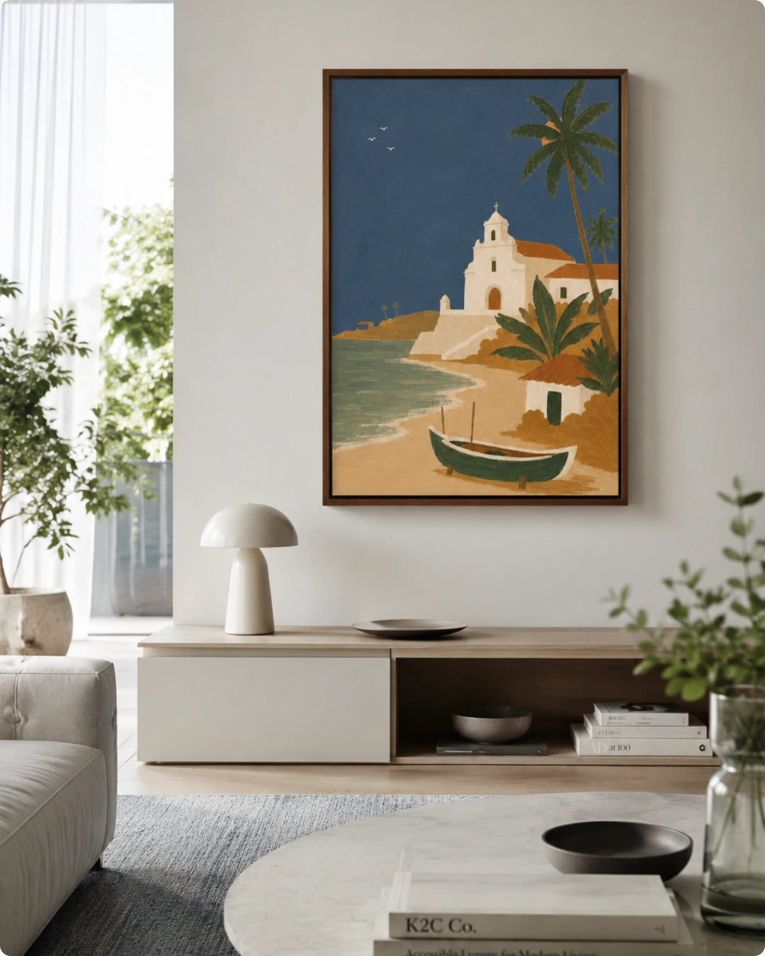 A framed art print depicting a tropical beach scene with a white church, palm trees, and a small boat, displayed on a white wall in a modern living room setting.