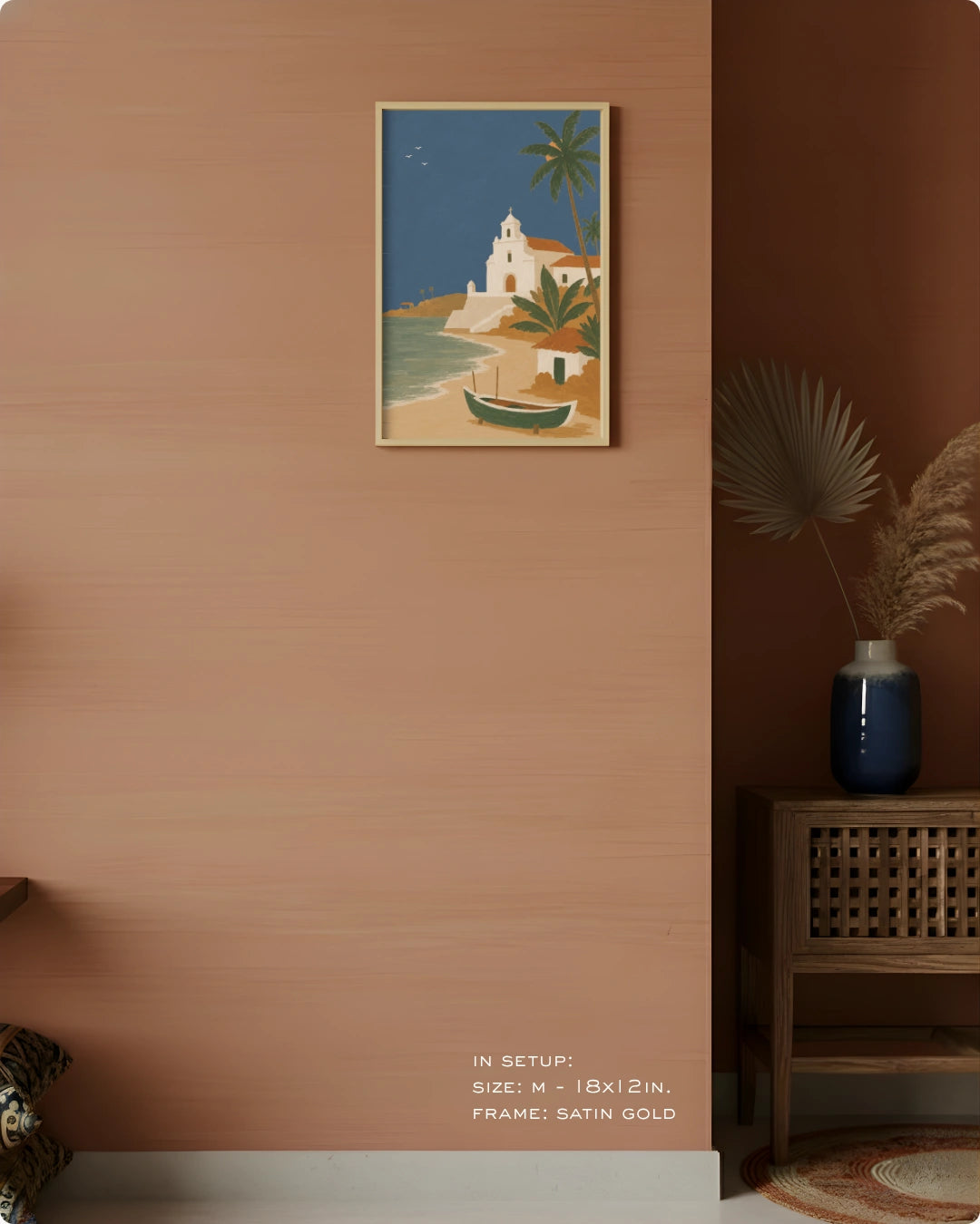 A framed art print depicting a Mediterranean coastal scene with a white church, palm trees, and a small boat, displayed on a terracotta-colored wall in a styled interior setting.