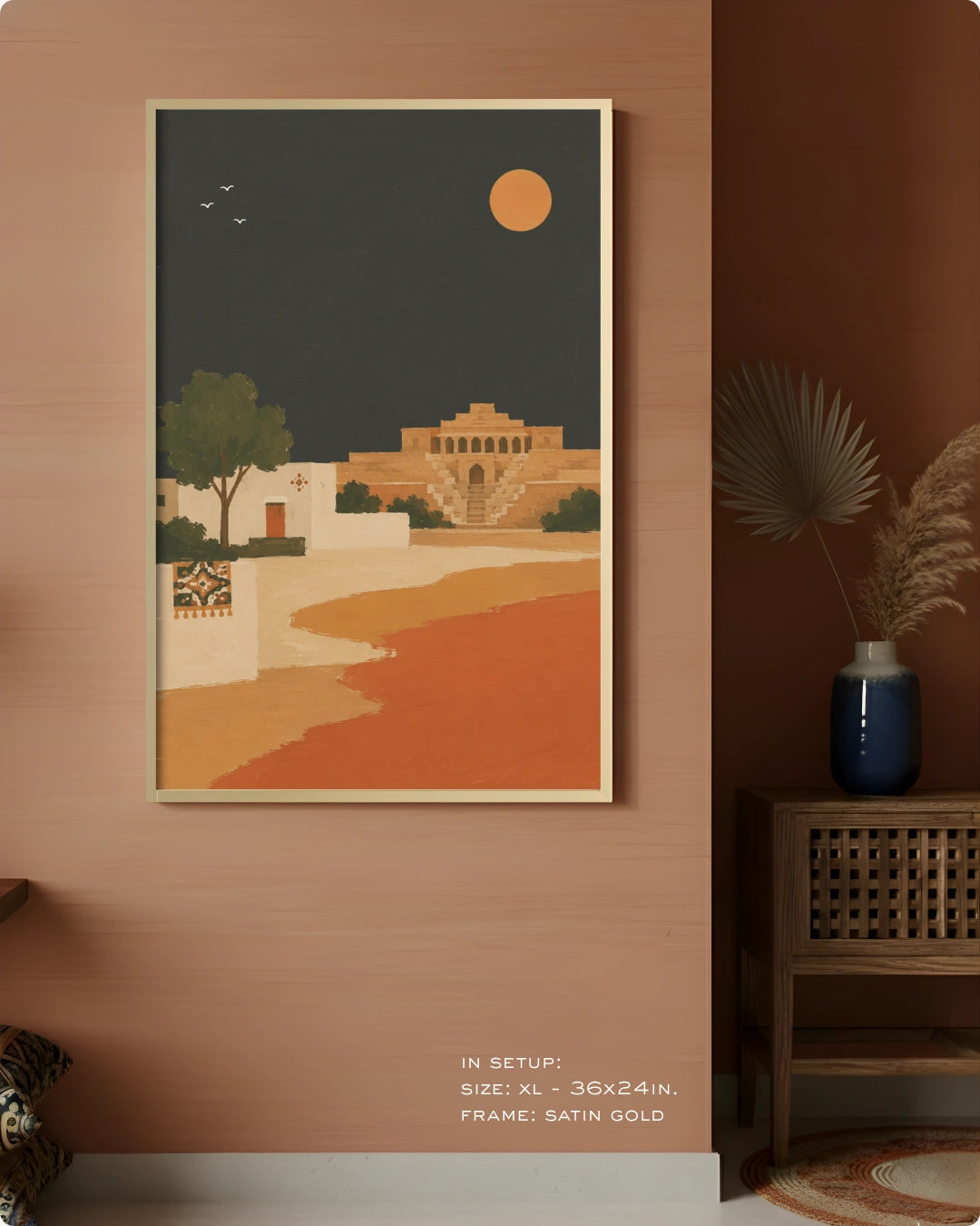 A framed art print featuring a retro-style desert landscape with a golden sun, a tree, and a building, displayed on a warm terracotta wall in a styled interior setting.
