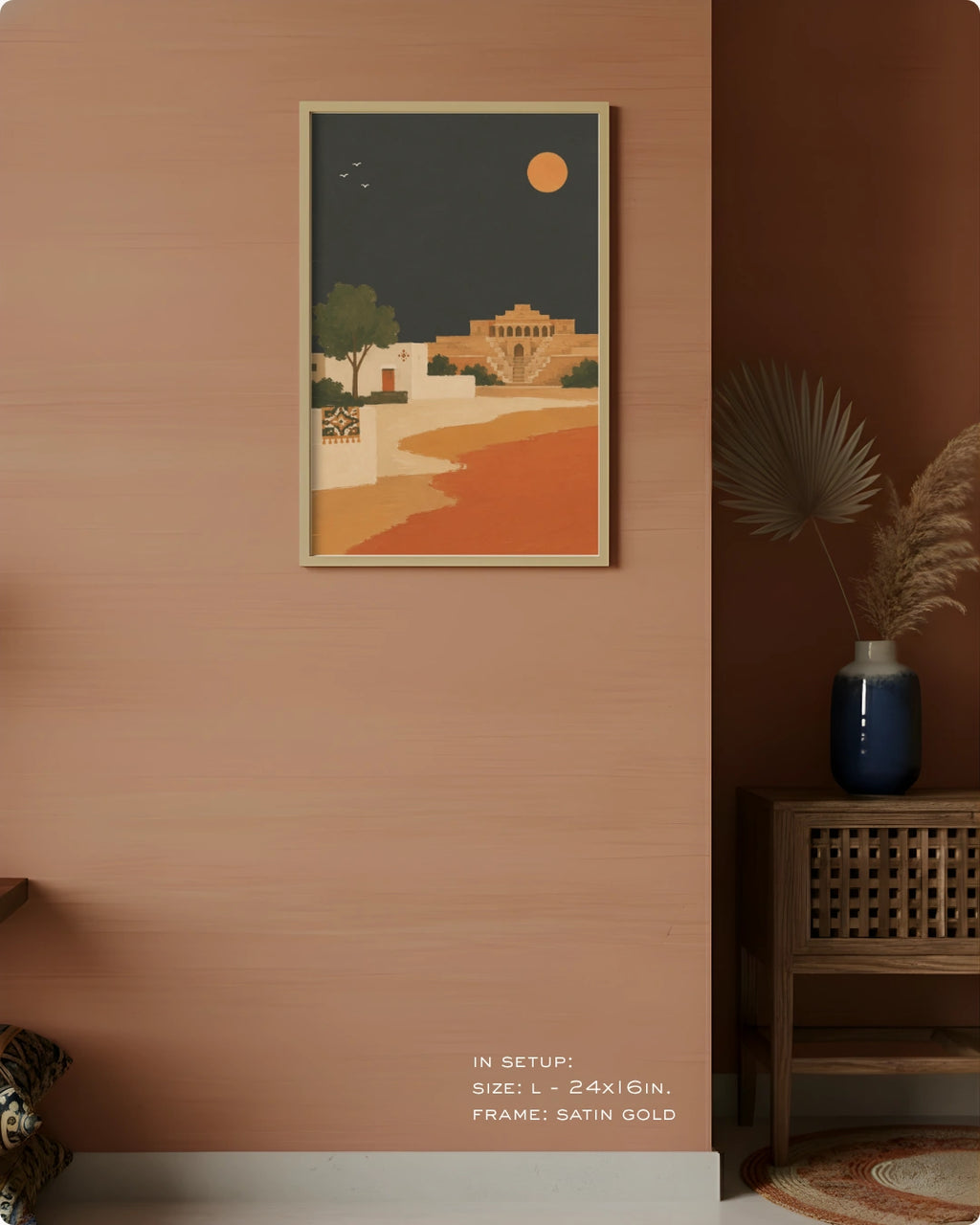 A framed art print featuring a retro-style desert landscape at night with a crescent moon and sun, displayed on a textured terracotta wall in a styled interior setting.