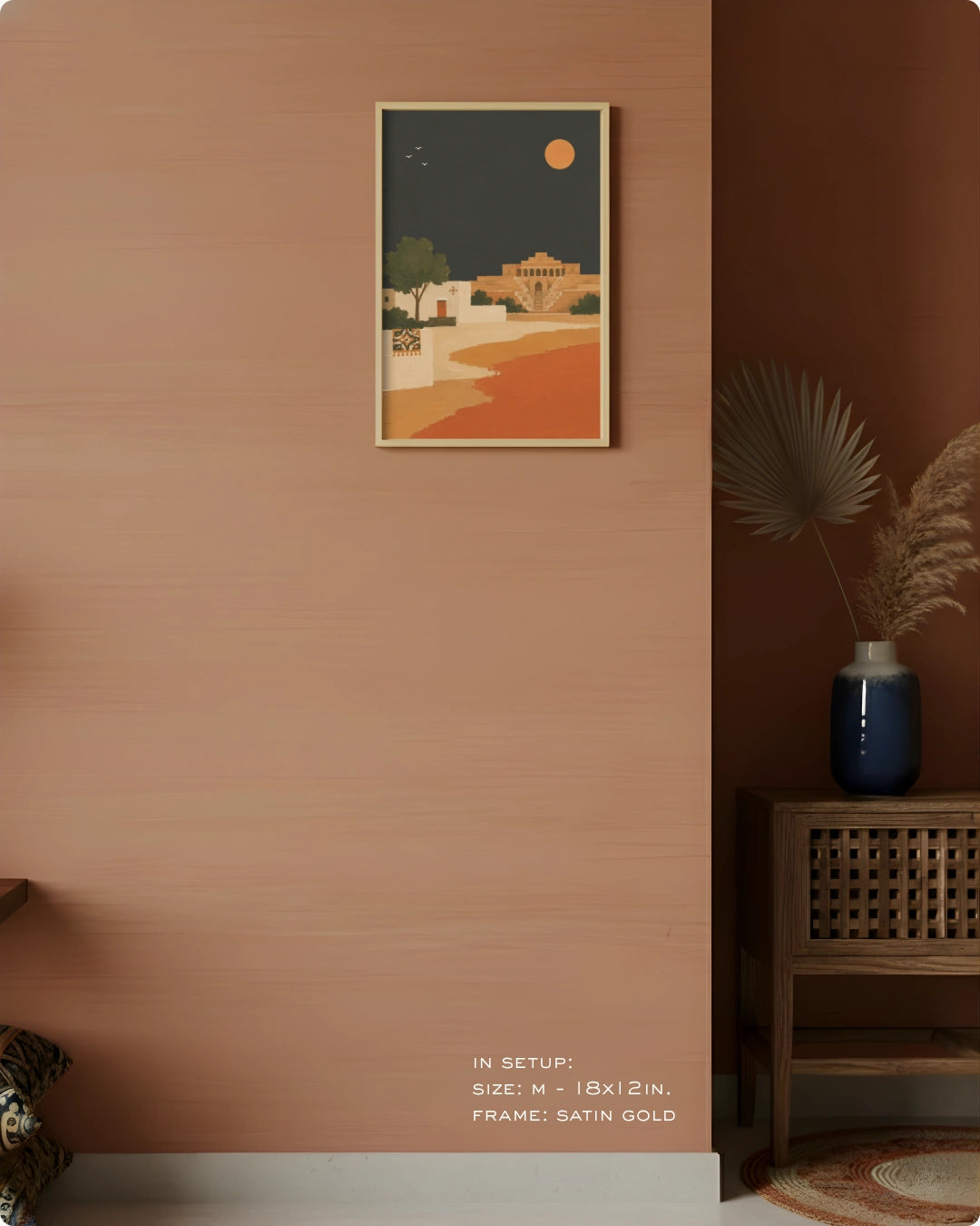 A framed art print featuring a retro-style desert landscape with a yellow sun and buildings under a dark sky, displayed on a terracotta-colored wall in a styled interior setting.