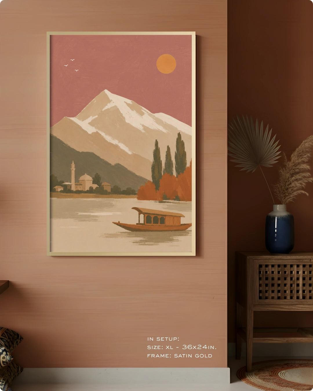 A framed art print featuring a retro-style landscape illustration with a snow-capped mountain, lake, small boat, and sun, displayed on a warm terracotta wall in a styled interior setting.