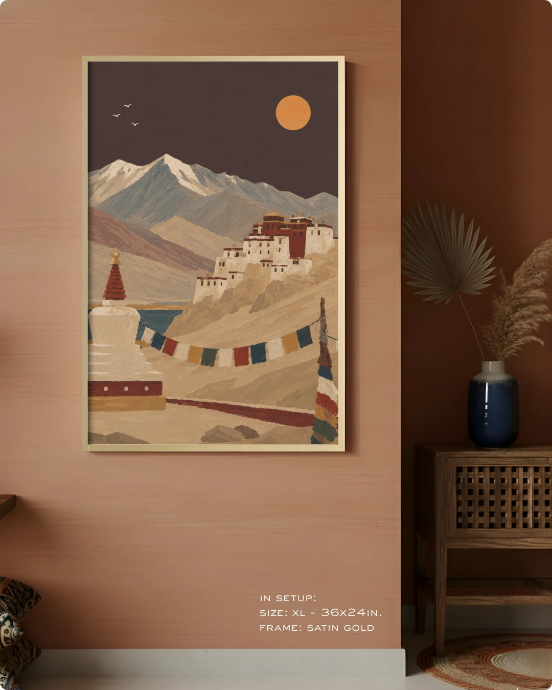 A framed art print depicting a scenic mountain landscape with a white stupa, prayer flags, and a golden sun, styled on a warm terracotta wall in a modern interior setting.